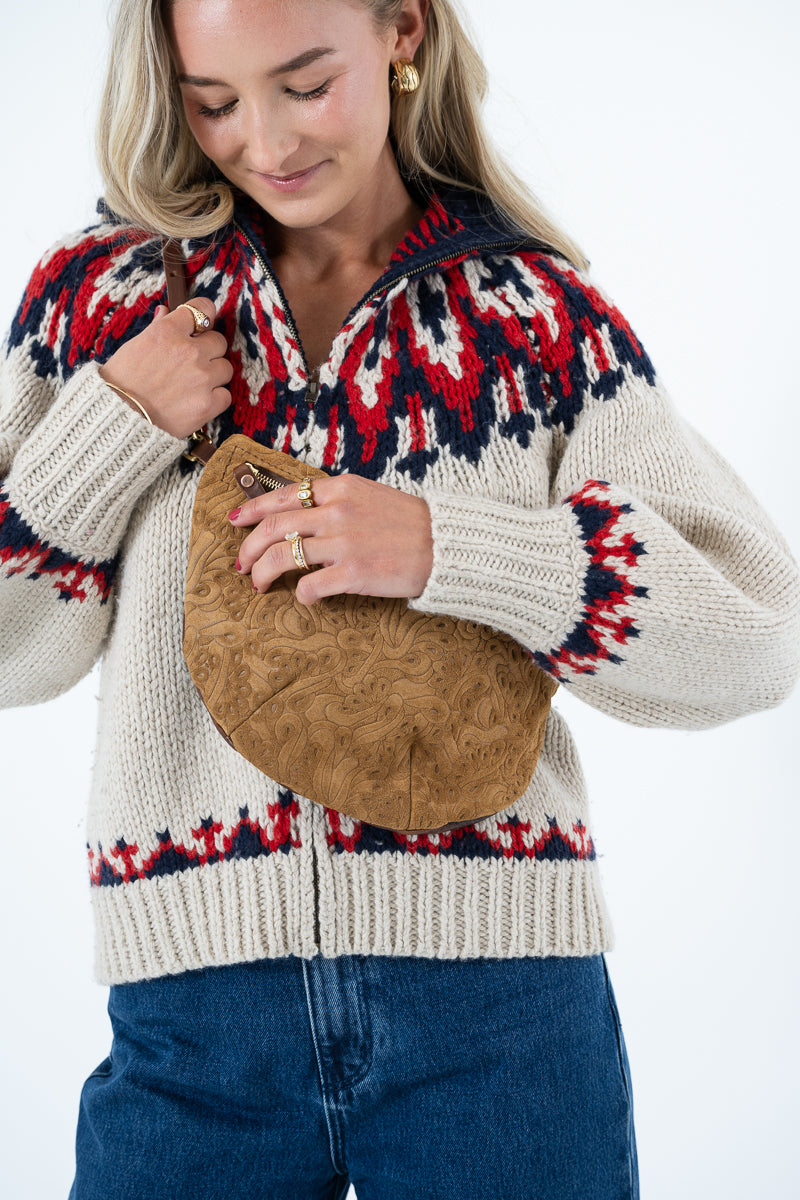 A woman wearing a cream knit zip-up sweater with a red and navy Fair Isle pattern, holding a brown textured suede crossbody bag, paired with blue jeans against a white background. Handmade by Meanwhile Back on the Farm in Lynchburg,VA