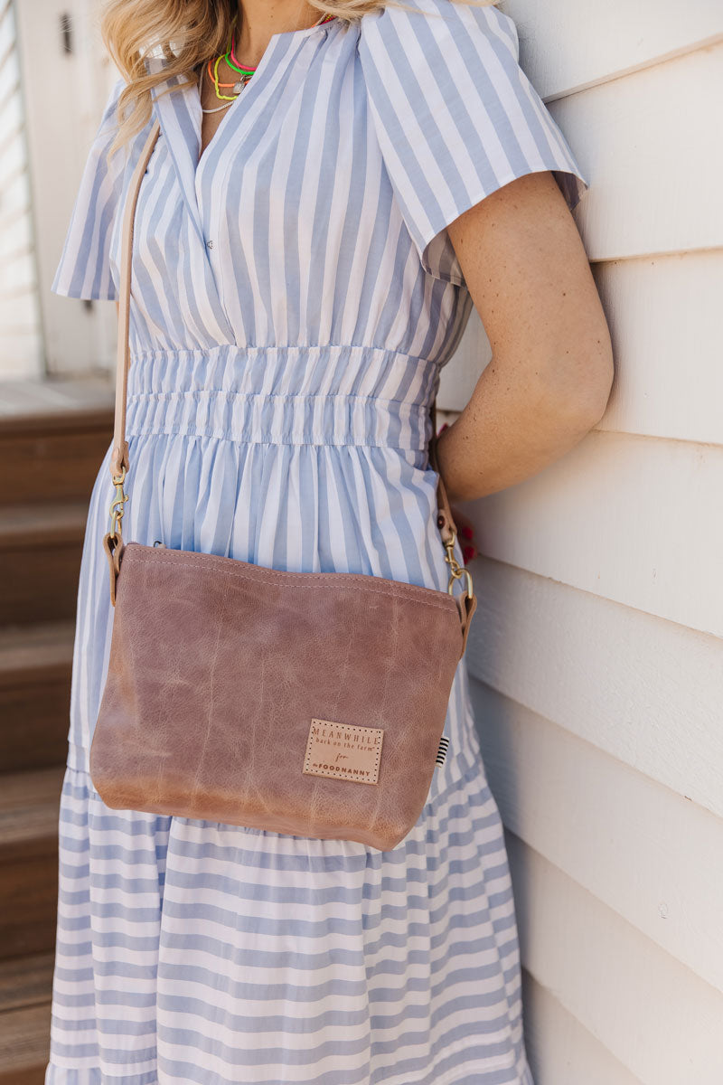 A woman wearing a soft pink bag with a tan body strap. 