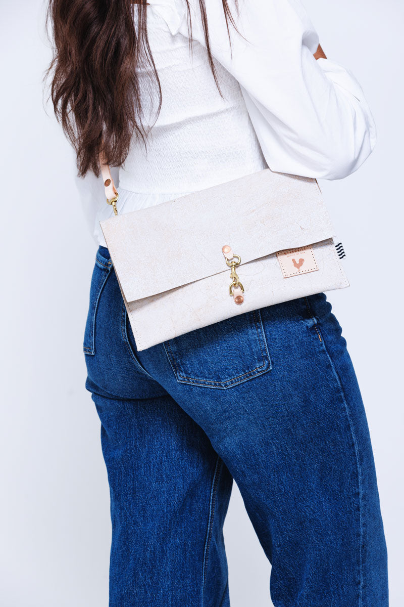 Picture of the back of a model who is wearing a birch white leather fold over clutch with a cream colored leather strap.
