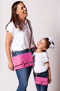 Mom and her daughter looking at each other both wearing matching pink fold over clutches.