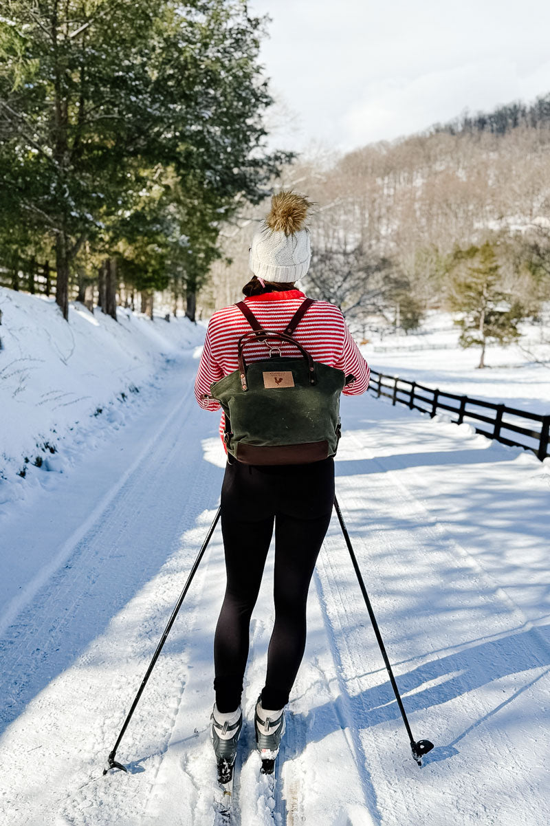 Model wearing olive colored back pack style bag with brown leather straps.