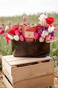 Red and brown leather bag filled with colorful tulips on a wooden crate in a field of tulips.