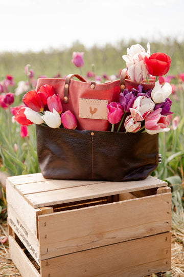 Red and brown leather bag filled with colorful tulips on a wooden crate in a field of tulips.