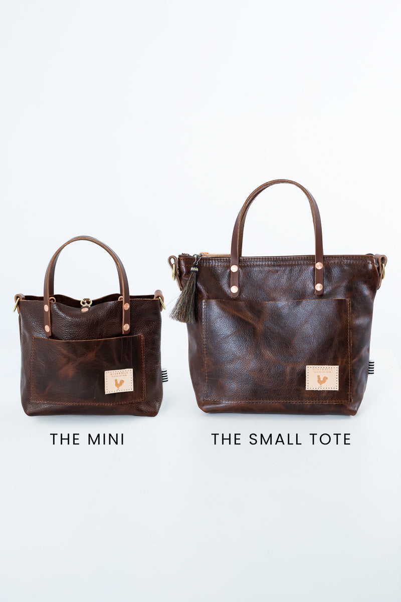 Two dark brown leather tote bags shown side by side on a light gray background, labeled 'THE MINI' and 'THE SMALL TOTE'. The larger bag on the right has double top handles, a front pocket, and a tassel detail, while the smaller bag on the left is a compact matching tote. Handmade by Meanwhile Back on the Farm in Lynchburg,VA