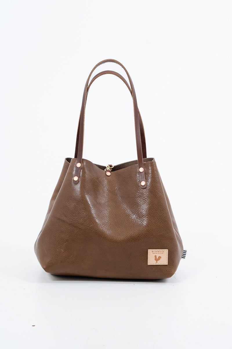 Brown leather handbag with a visible brand logo on a white background. Handmade by Meanwhile Back on the Farm in Lynchburg,VA