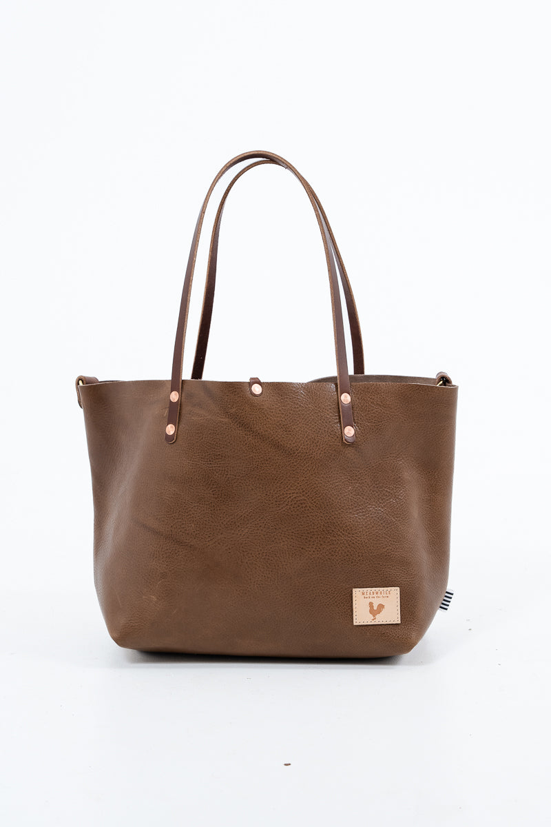 A chestnut brown tote bag with a visible brand logo on a white background. Handmade by Meanwhile Back on the Farm in Lynchburg,VA