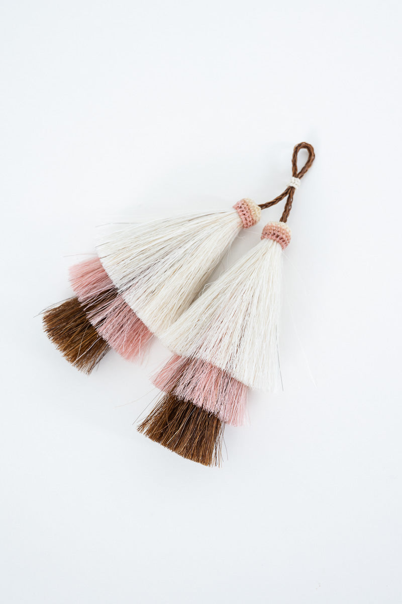 Five decorative tassel garlands with layered white, pink, and brown synthetic tassels, arranged on a clean white background. Proudly handcrafted by Meanwhile Back on the Farm in Lynchburg, Va.