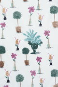 A repeating botanical pattern on a white background featuring potted topiary trees, pink flowers, and a central teal leafy arrangement in a dark urn. Proudly handcrafted by Meanwhile Back on the Farm in Lynchburg, Va.