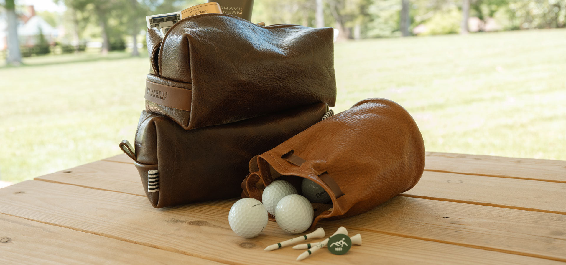 Brown leather golf bag with golf balls and tees on a wooden table outdoors.