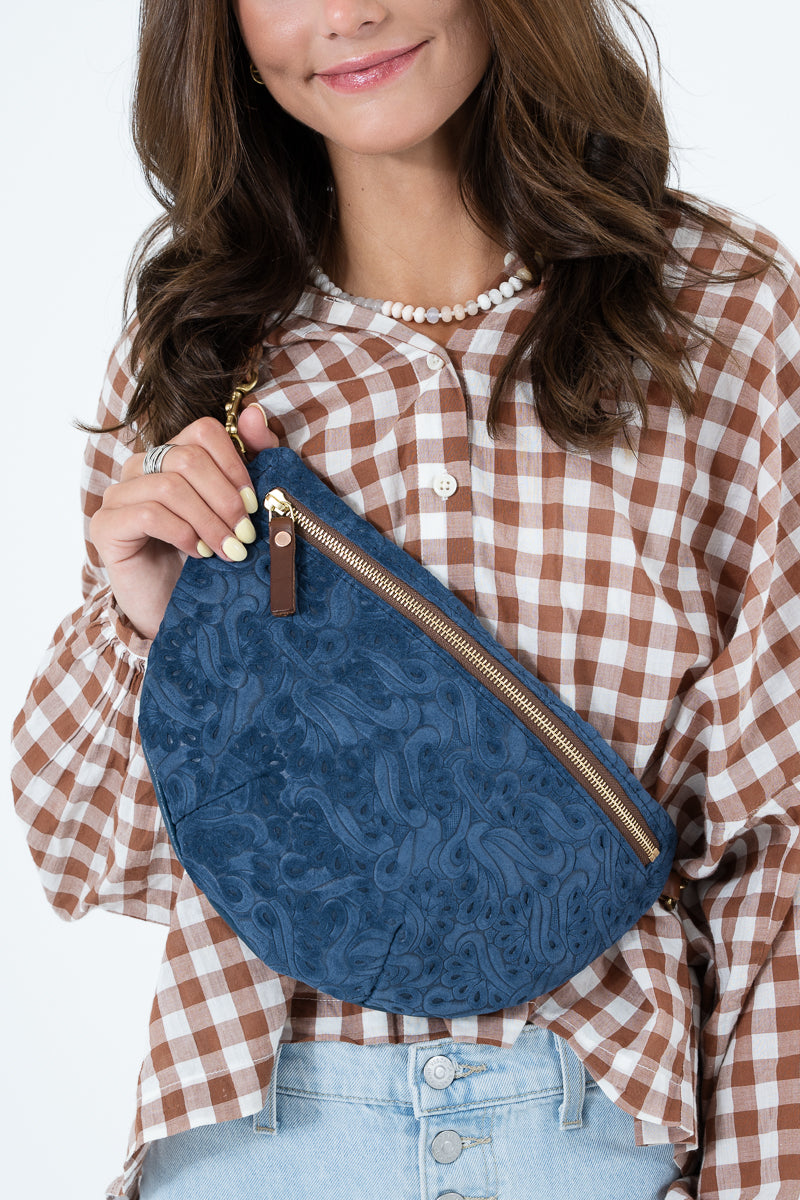 A woman wearing a brown and white gingham shirt models a blue paisley-patterned crescent-shaped clutch bag with a gold zipper. Handcrafted by Meanwhile Back on the Farm in Lynchburg, Va.