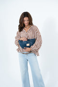 A woman wearing a brown and beige gingham shirt and light blue jeans holds a navy blue leather clutch bag with a gold logo patch. Handcrafted by Meanwhile Back on the Farm in Lynchburg, Va.