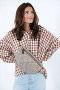A woman wearing a brown and white gingham shirt and light blue jeans, carrying a taupe textured leather crescent crossbody bag with gold-tone hardware. Handcrafted by Meanwhile Back on the Farm in Lynchburg, Va.