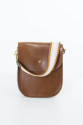 A brown leather crossbody bag with a wide, striped fabric strap in white, brown, and tan, featuring gold-tone hardware on a white background. Handmade by Meanwhile Back on the Farm in Lynchburg,VA