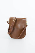 A brown textured leather crossbody bag with a flap closure, adjustable strap, and gold-tone hardware, photographed on a clean white background. Handmade by Meanwhile Back on the Farm in Lynchburg,VA
