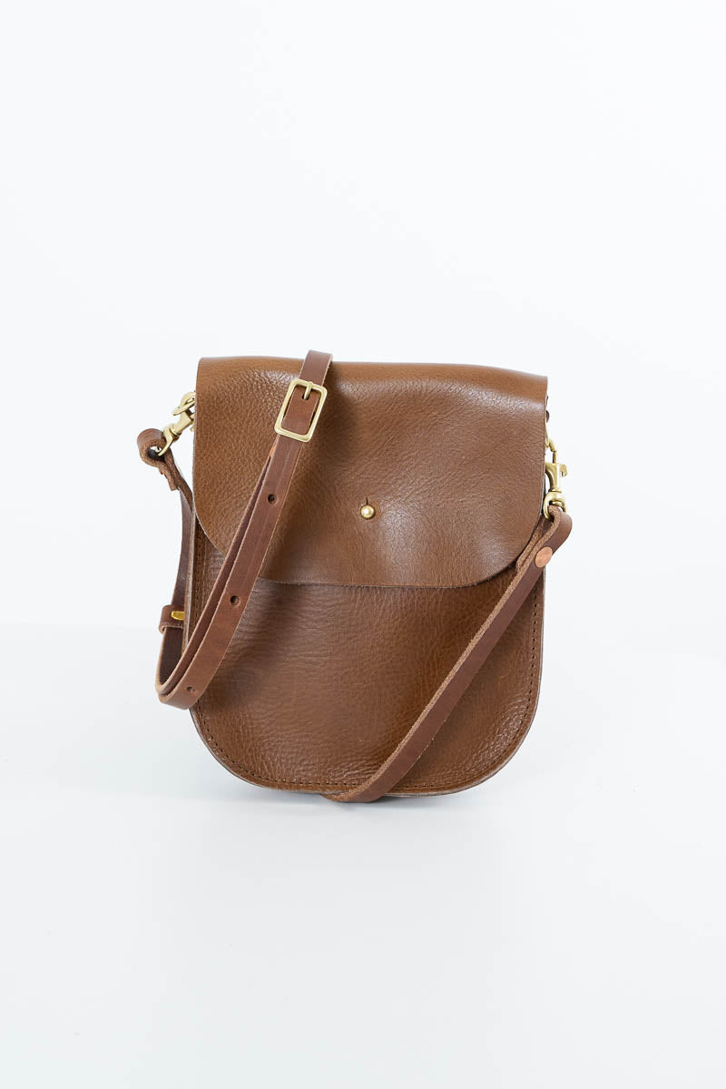 A brown textured leather crossbody bag with a flap closure, adjustable strap, and gold-tone hardware, photographed on a clean white background. Handmade by Meanwhile Back on the Farm in Lynchburg,VA
