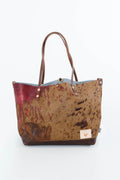 A tote bag featuring a mottled brown and beige cowhide pattern, a red painted section on the left, a light blue interior lining, and dark brown leather handles and trim, shown on a white background. Handcrafted by Meanwhile Back on the Farm in Lynchburg, Va.
