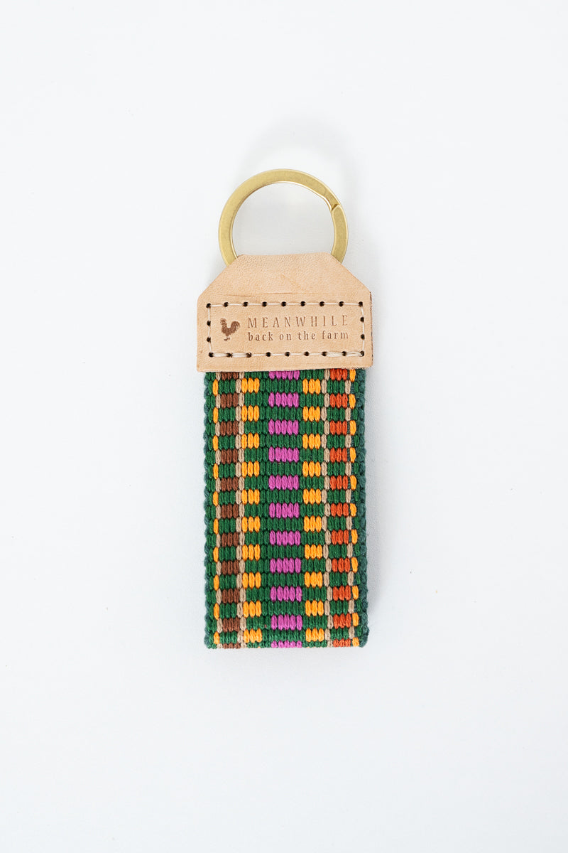 Colorful webbing key fob with shades of green, pink, orange, and gold and the Meanwhile Back on the Farm logo