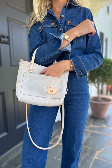 Woman holding the birch white shoulder strap bag with the meanwhile logo and a brown body strap.