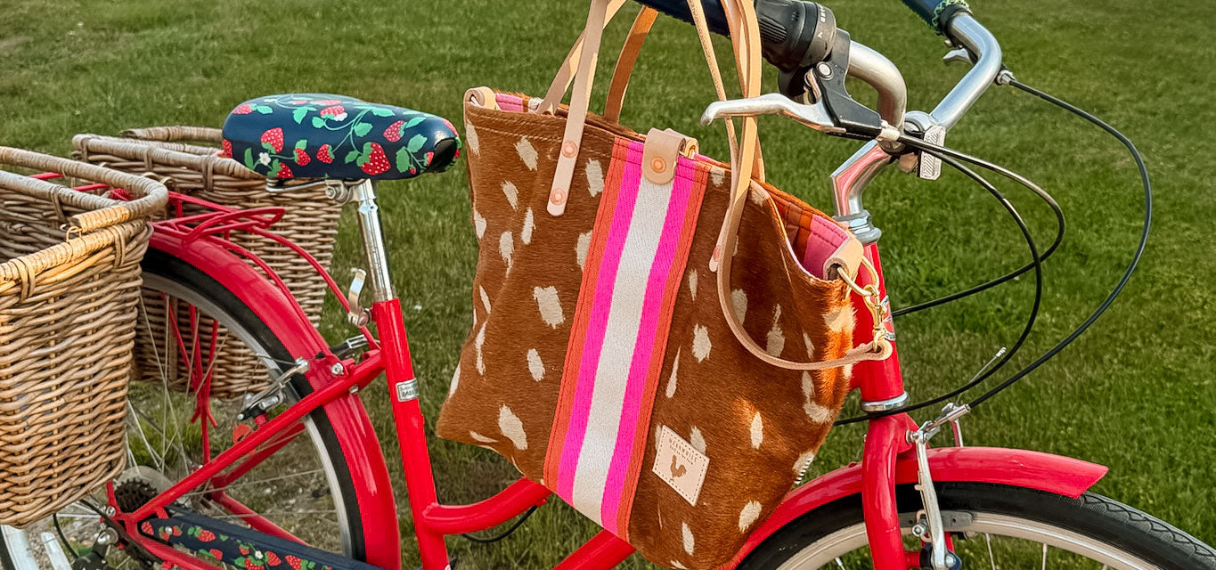Red bicycle with a brown cowhide bag with a pink orange and white stripe in the middle