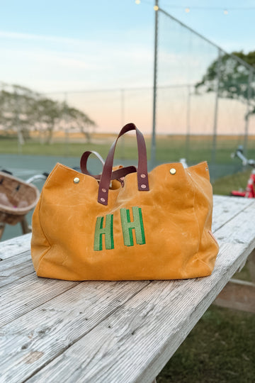 Yellow Meanwhile Back on the Farm tote bag with 'HH' initials on a wooden surface outdoors