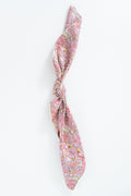 A pink silk scarf with a dense multicolor floral and paisley print, tied in a knot and displayed vertically against a clean white background. Handmade by Meanwhile Back on the Farm in Lynchburg,VA