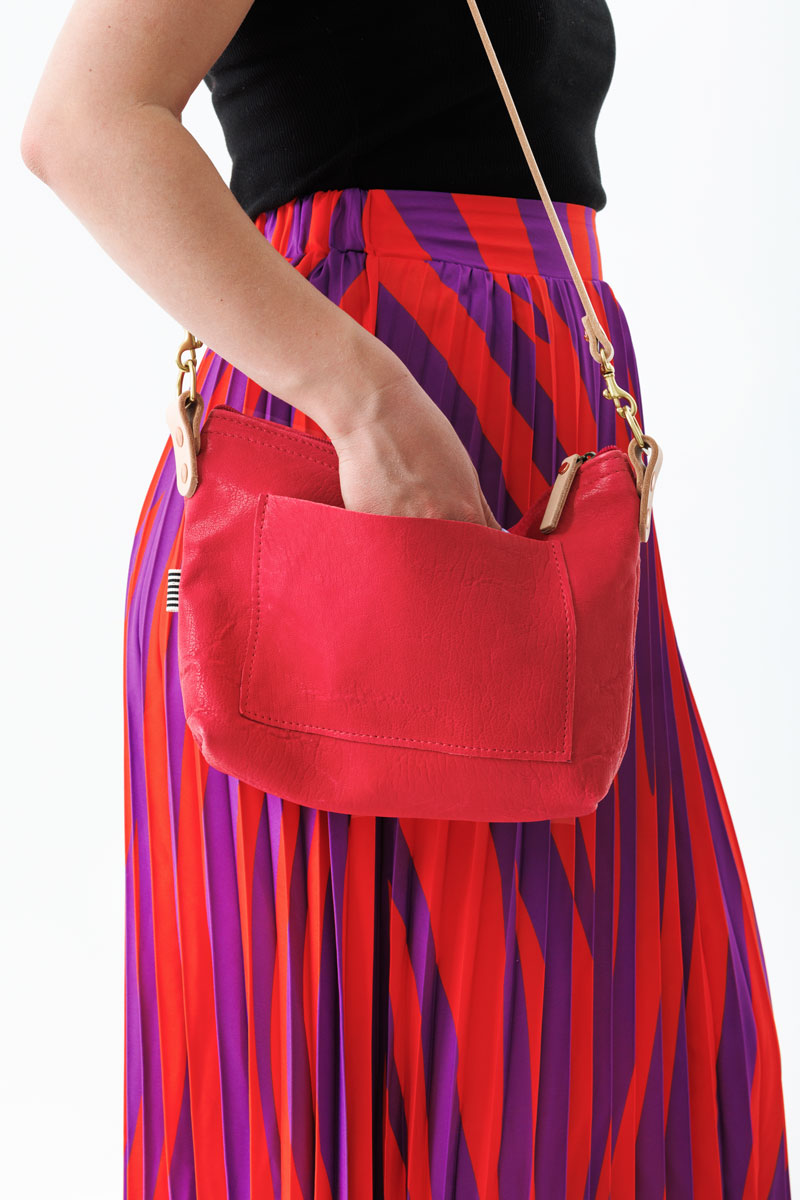 Woman holding the bright pink bag with an outside pocket and a brown body strap.