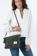 A woman wearing a white eyelet blouse and blue jeans carries an olive green waxed canvas and brown leather crossbody bag  a small leather patch on the front. Handmade by Meanwhile Back on the Farm in Lynchburg,VA