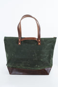 A green waxed canvas tote bag with dark brown leather handles and a matching dark brown leather base, shown against a plain white background. Handmade by Meanwhile Back on the Farm in Lynchburg,VA