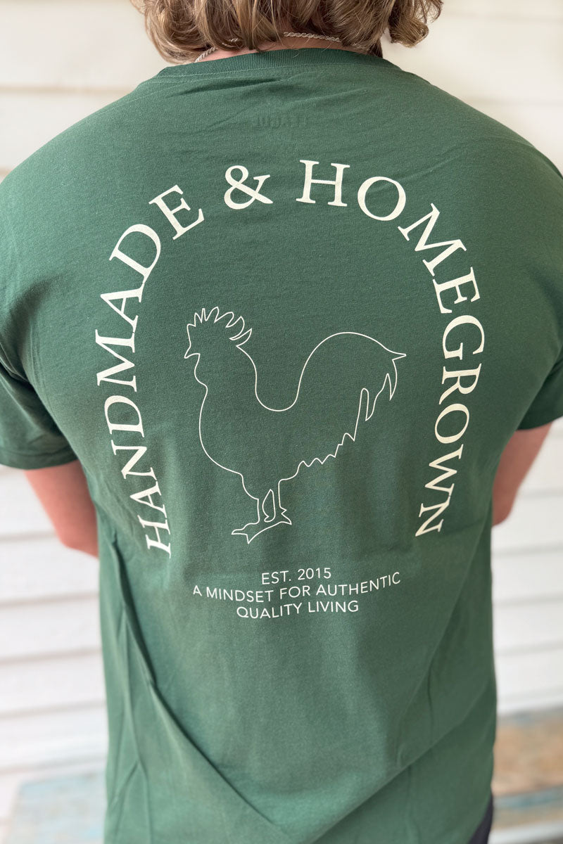 Male model wearing a hunter green reading 'Handmade & Homegrown' est 2015 A Mindset For Authentic Quality Living. Company's large rooster logo is outlined in the center