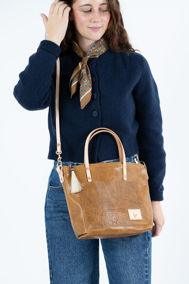 Woman standing in front of a store holding a small brown leather tote and a bouquet of pink/white flowers 