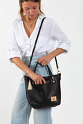 A woman holding a black bag with a body strap with a tan tassel and meanwhile logo.