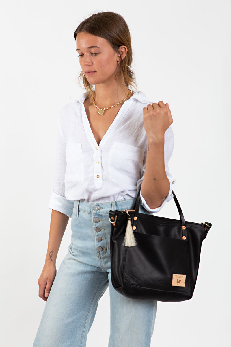 A woman holding a black short strapped bag with a tan tassel and meanwhile logo.
