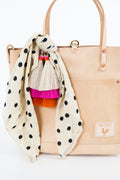 A light beige leather tote bag with gold-tone hardware, featuring a cream-colored scarf with black polka dots draped over the front. The scarf has a tassel charm with cream, pink, and orange fringe. Handmade by Meanwhile Back on the Farm in Lynchburg,VA
