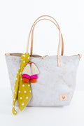 A light gray leather tote bag with tan leather handles, decorated with a yellow and white polka dot scarf and colorful tassels, set against a plain white background. Handmade by Meanwhile Back on the Farm in Lynchburg,VA