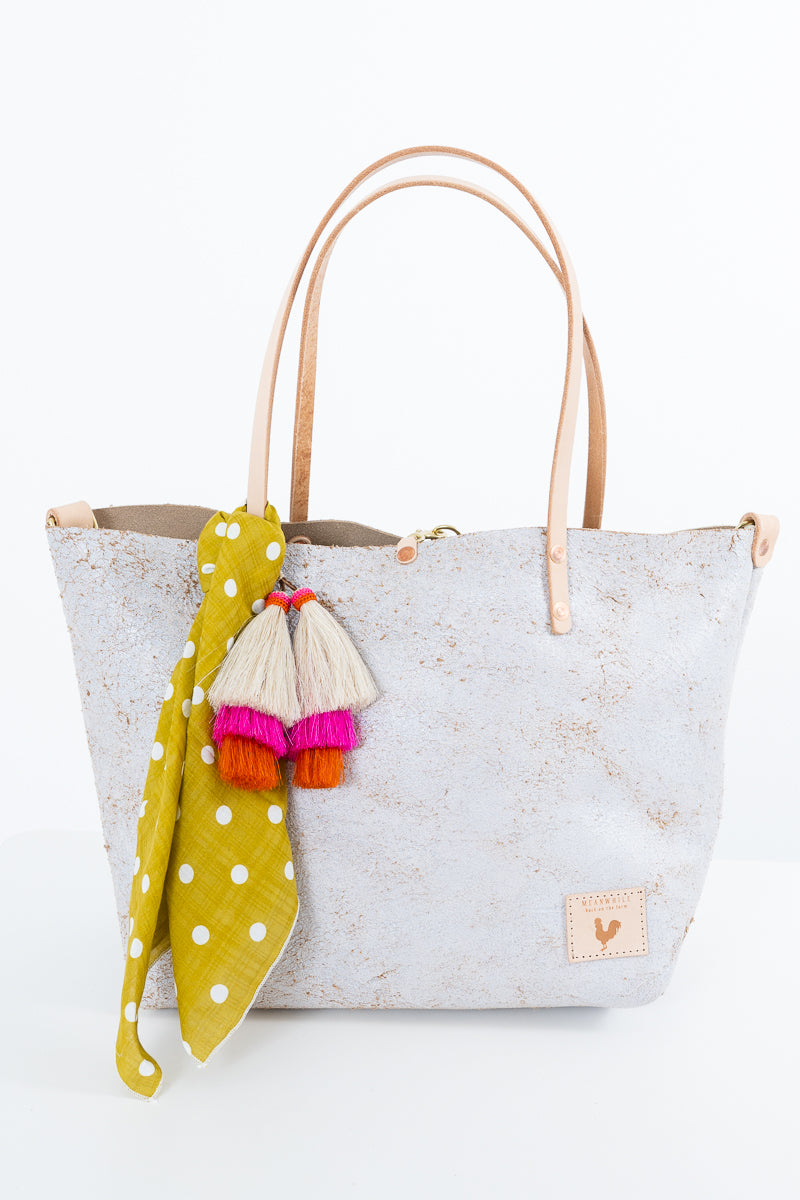 A light gray leather tote bag with tan leather handles, decorated with a yellow and white polka dot scarf and colorful tassels, set against a plain white background. Handmade by Meanwhile Back on the Farm in Lynchburg,VA