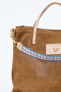 Brown leather Meanwhile Back on the Farm bag with a blue and white webbing strap