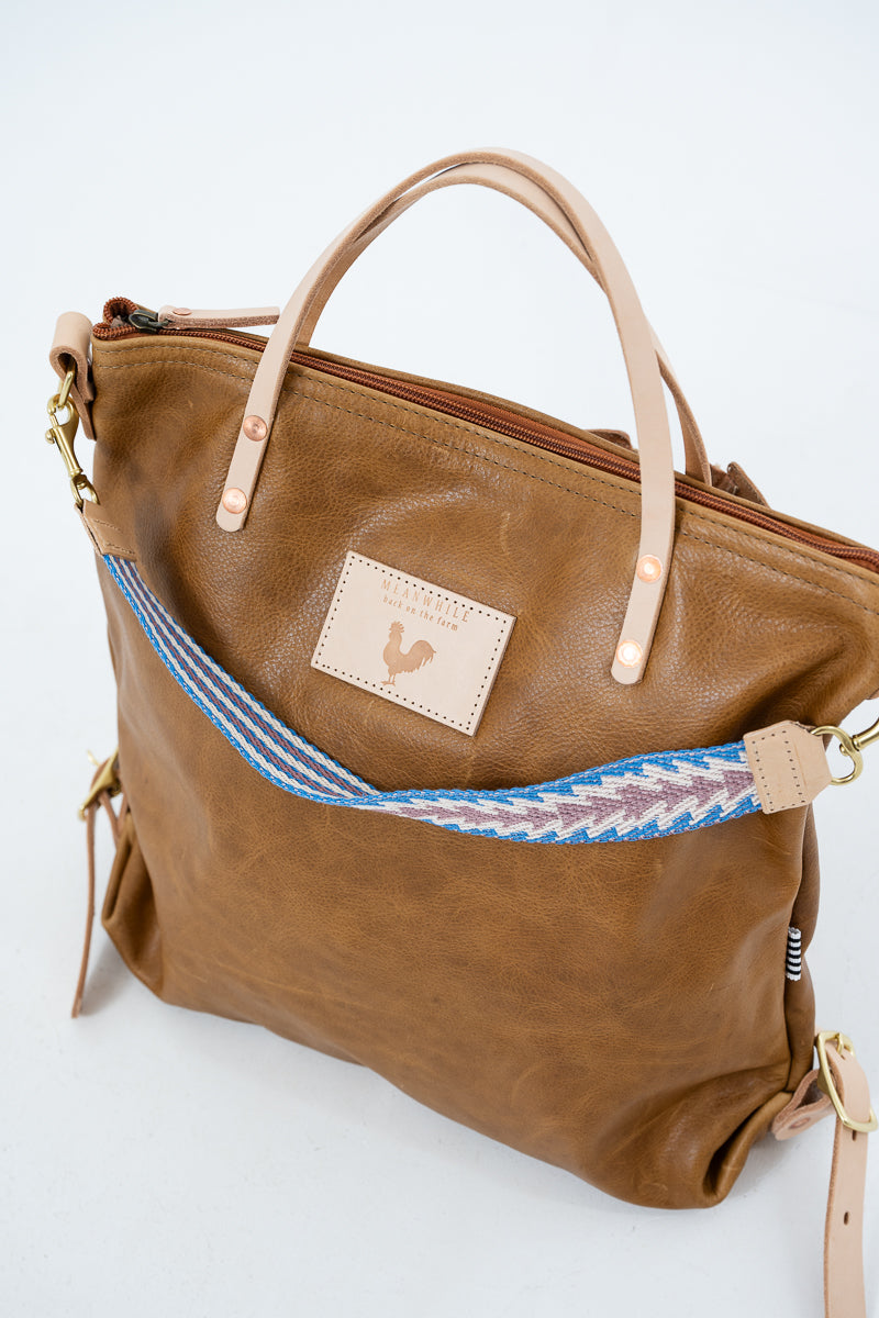 Brown leather Meanwhile Back on the Farm bag with a blue and white webbing strap