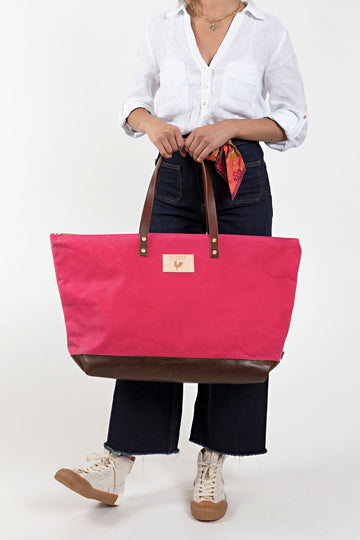 Woman holding the bright pink weekend bag with dark brown straps and meanwhile logo.