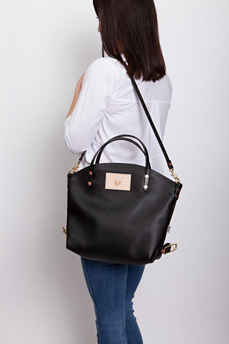 A woman wearing the black backpack with black straps and the meanwhile logo.