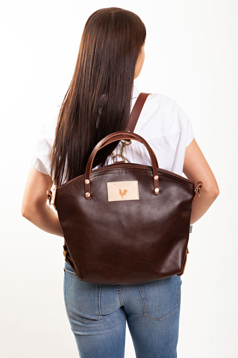 A woman wearing the mocha brown backpack with the meanwhile logo.