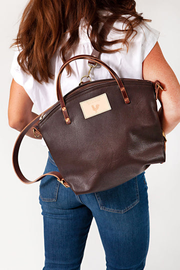 A woman wearing the mocha brown backpack with brown straps and the meanwhile logo.