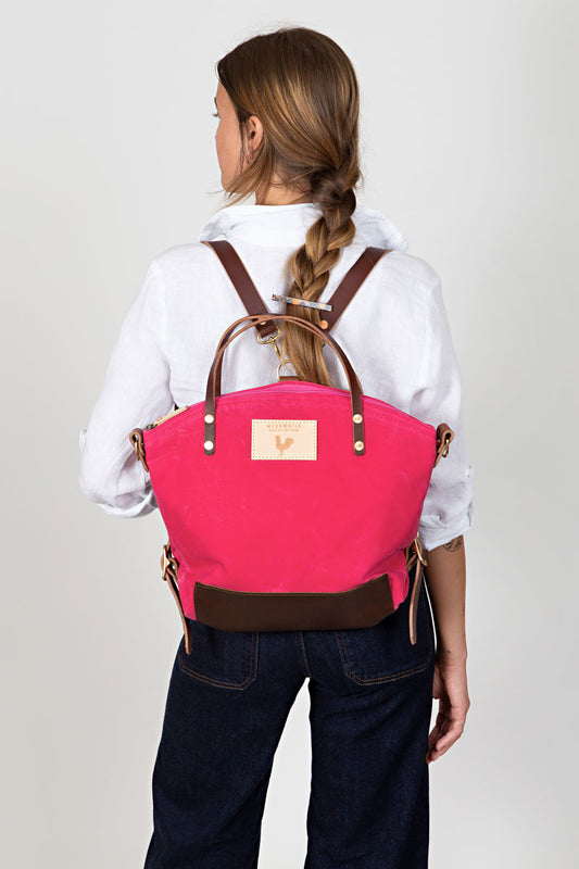 A woman wearing the bright pink backpack with meanwhile logo and brown straps.