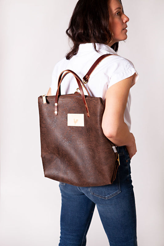 Woman wearing the birch mocha backpack with meanwhile logo and dark brown straps.