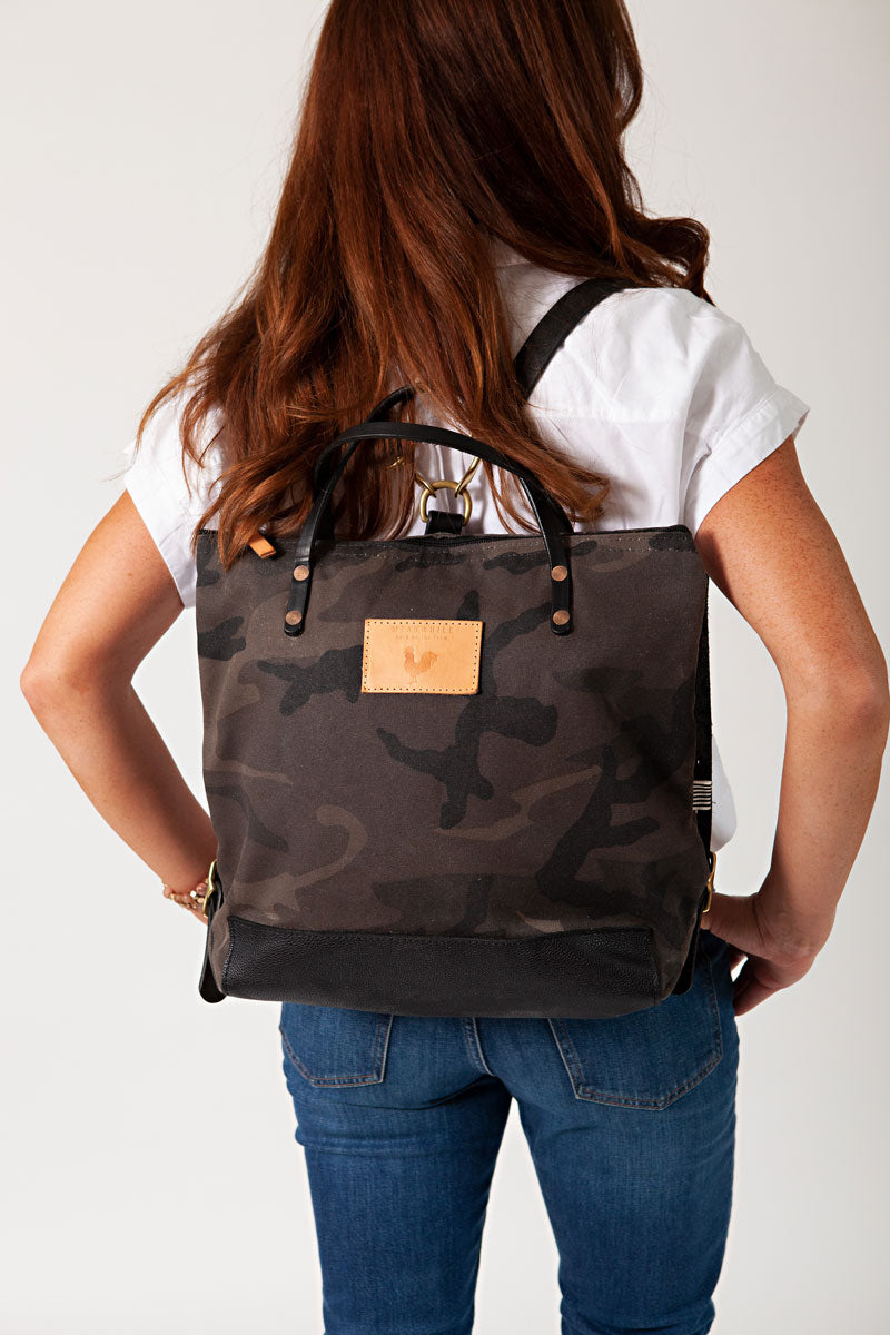 A women wearing the graphite camouflage backpack with black straps and the meanwhile logo.