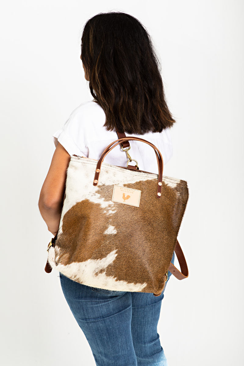 A woman wearing the hair on hide backpack with brown straps and the meanwhile logo.