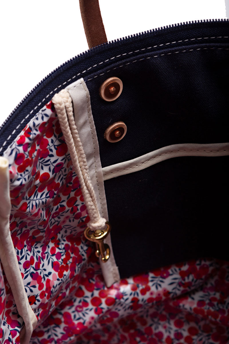 Picture of interior of navy bag. Bag is lined with a red floral print and a side pocket.