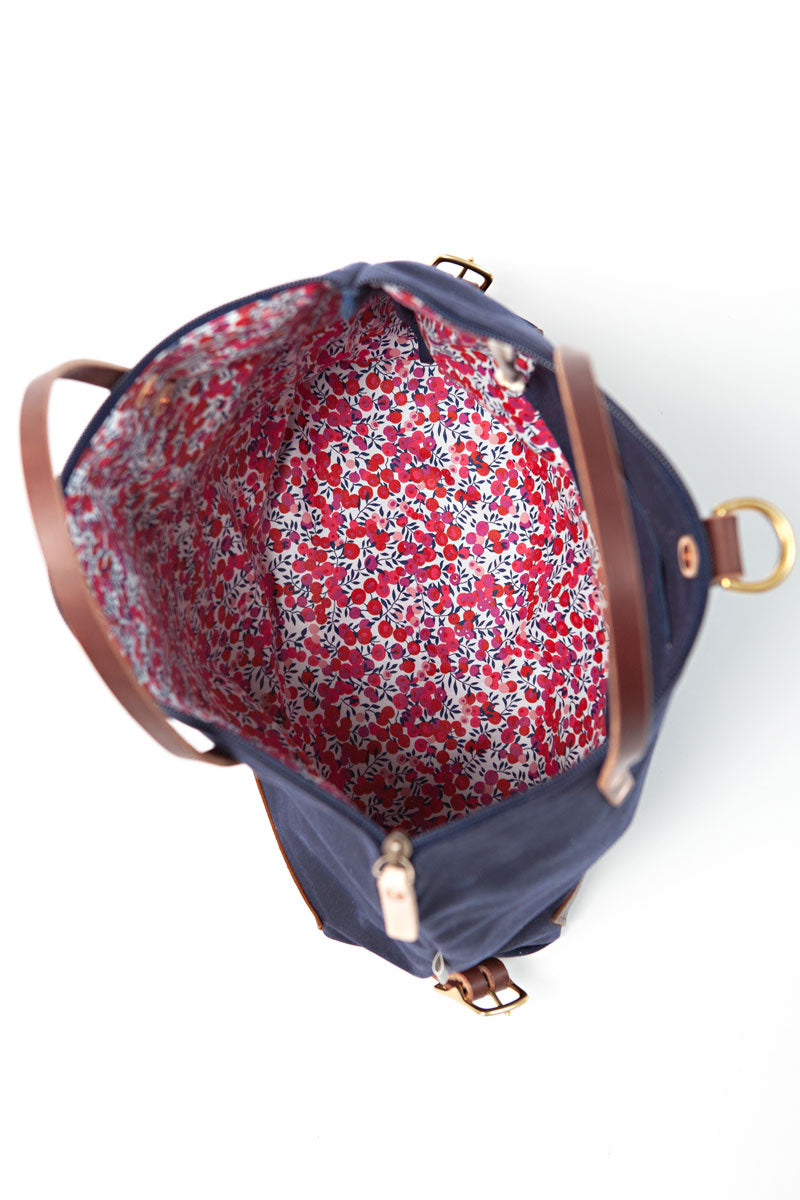 Picture of the interior of a navy blue bag with dark brown leather straps. Interior is lined with red floral fabric.