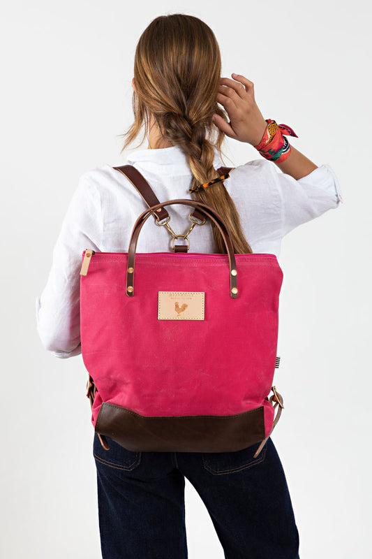 A woman wearing the bright pink backpack with dark brown straps and the meanwhile logo.