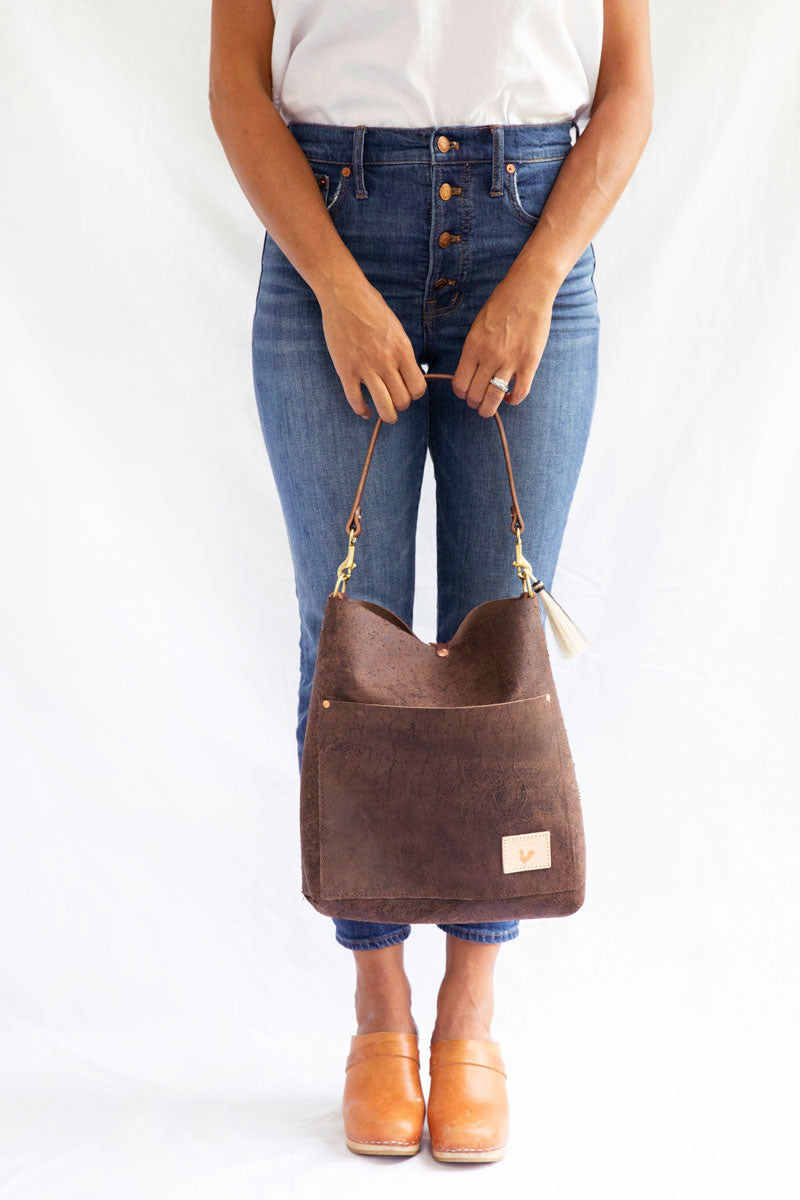 Woman reaching in the outside pocket of the birch mocha bag with meanwhile logo and dark brown straps.