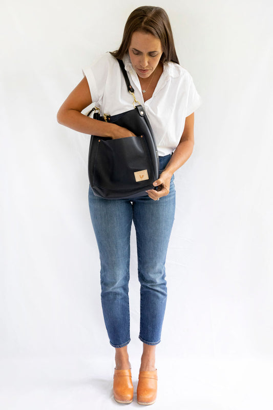 A woman holding the black bag with a black shoulder strap and meanwhile logo.